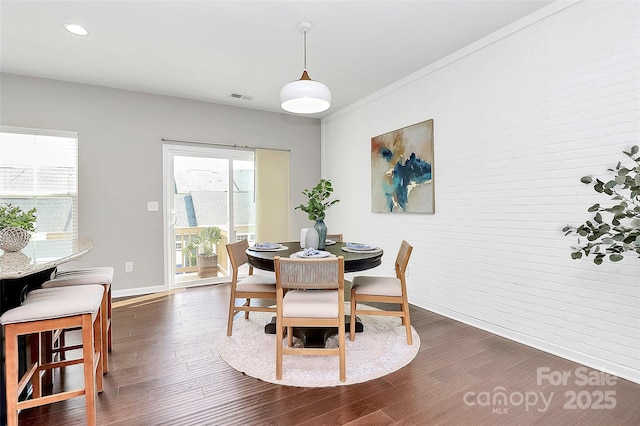 dining space featuring brick wall, dark hardwood / wood-style flooring, and crown molding