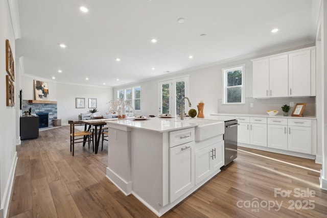 kitchen featuring white cabinets, an island with sink, sink, stainless steel dishwasher, and crown molding