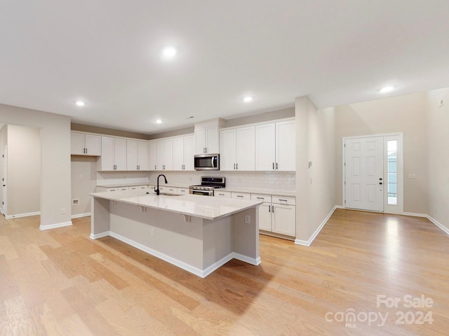 kitchen with a kitchen bar, stainless steel appliances, an island with sink, white cabinetry, and light wood-type flooring