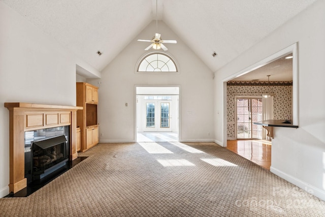 unfurnished living room featuring ceiling fan, light colored carpet, a fireplace with flush hearth, baseboards, and high vaulted ceiling