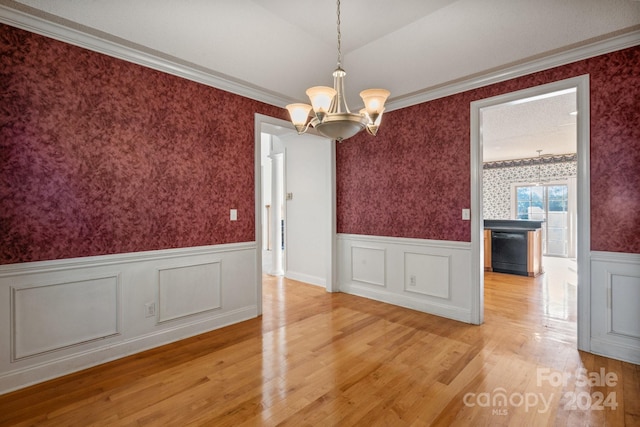 unfurnished dining area with wallpapered walls, a notable chandelier, wainscoting, and light wood-style flooring