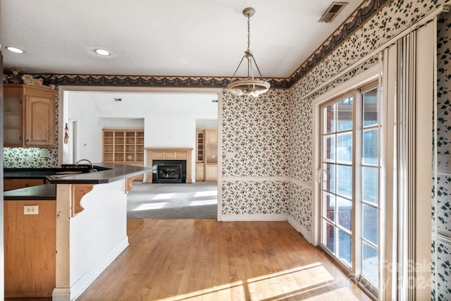kitchen featuring a fireplace, dark countertops, light wood finished floors, and wallpapered walls