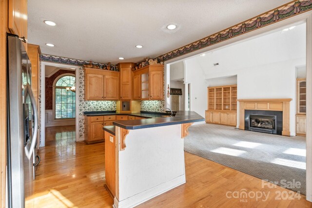 kitchen with a breakfast bar area, dark countertops, a peninsula, stainless steel fridge, and light wood-style flooring