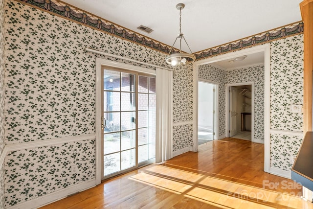 unfurnished dining area featuring visible vents, crown molding, an inviting chandelier, wood finished floors, and wallpapered walls