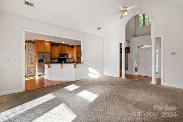 unfurnished living room with ornate columns, high vaulted ceiling, light colored carpet, and visible vents