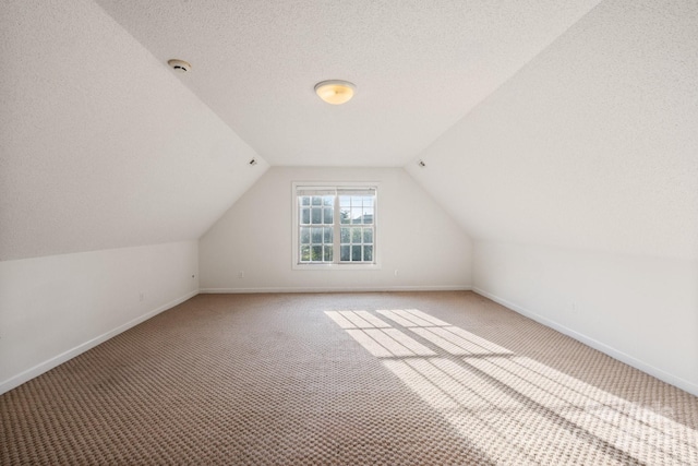additional living space with baseboards, light carpet, vaulted ceiling, and a textured ceiling