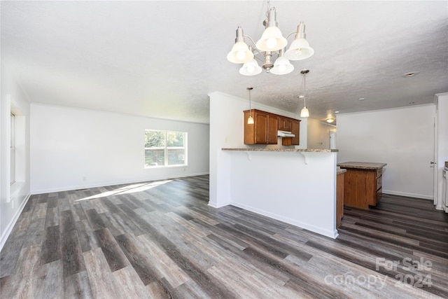 kitchen featuring hanging light fixtures, light stone counters, kitchen peninsula, dark hardwood / wood-style flooring, and a notable chandelier