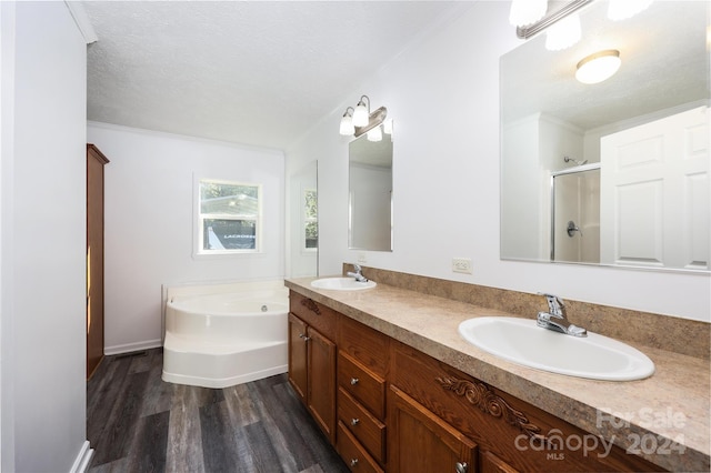 bathroom with a textured ceiling, independent shower and bath, hardwood / wood-style floors, ornamental molding, and vanity