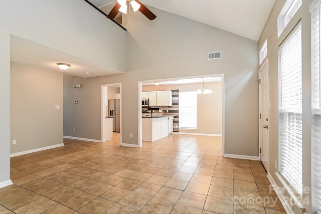 unfurnished living room with high vaulted ceiling, a wealth of natural light, light tile patterned floors, and ceiling fan with notable chandelier