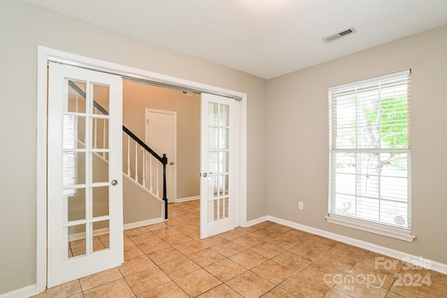 tiled empty room with french doors and a textured ceiling