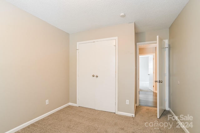 unfurnished bedroom with a textured ceiling, light carpet, and a closet