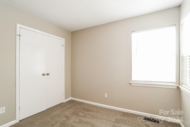 unfurnished bedroom featuring a textured ceiling, a closet, and carpet floors