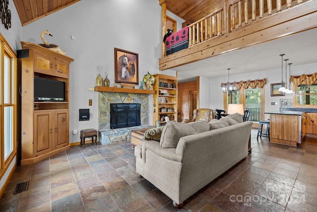 living room with high vaulted ceiling, wooden ceiling, a chandelier, and a stone fireplace