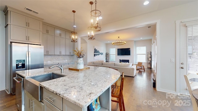 kitchen featuring a fireplace, decorative backsplash, a kitchen island with sink, and hanging light fixtures