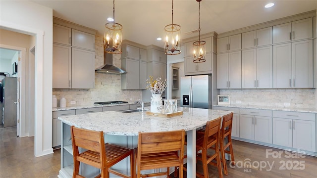 kitchen featuring a kitchen island with sink, hanging light fixtures, wall chimney exhaust hood, decorative backsplash, and appliances with stainless steel finishes