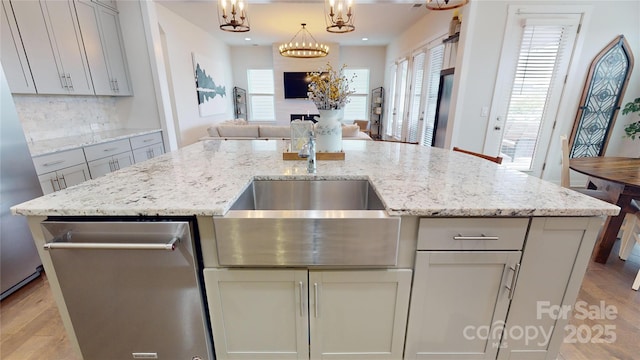 kitchen featuring pendant lighting, light stone countertops, backsplash, and an island with sink