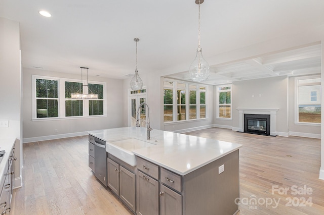 kitchen with sink, stainless steel dishwasher, decorative light fixtures, a kitchen island with sink, and light hardwood / wood-style floors