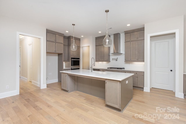 kitchen featuring a large island, decorative light fixtures, wall chimney exhaust hood, stainless steel appliances, and light hardwood / wood-style floors