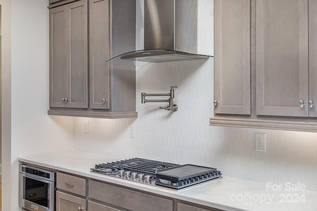 kitchen with wall chimney exhaust hood, stainless steel appliances, and tasteful backsplash