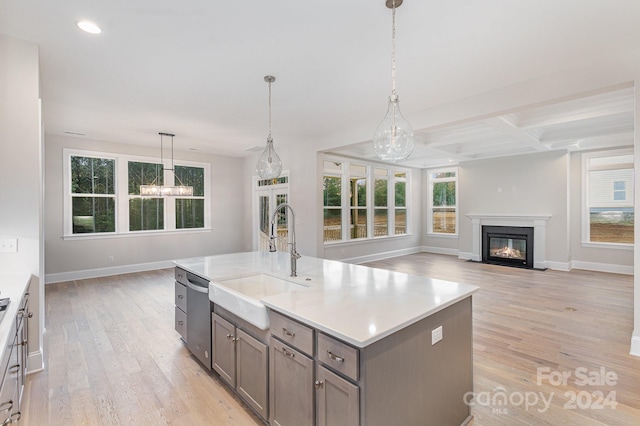 kitchen featuring pendant lighting, sink, stainless steel dishwasher, a center island with sink, and light wood-type flooring