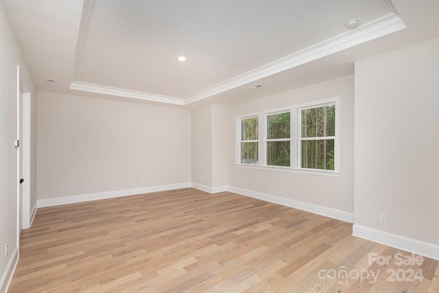 unfurnished room with light wood-type flooring, a raised ceiling, and crown molding