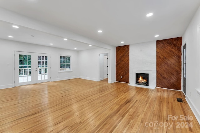 unfurnished living room featuring light hardwood / wood-style flooring, french doors, and a brick fireplace