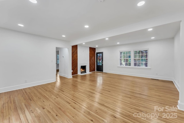 unfurnished living room featuring light wood-style floors, recessed lighting, a large fireplace, and baseboards