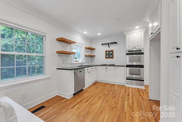 kitchen with open shelves, stainless steel appliances, dark countertops, white cabinetry, and a sink