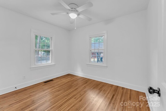 spare room featuring baseboards, visible vents, ceiling fan, and wood finished floors