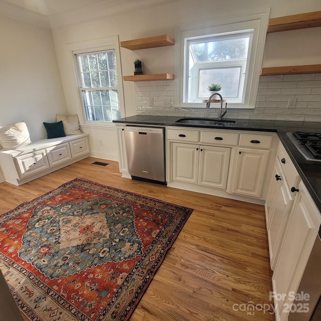 kitchen featuring a sink, appliances with stainless steel finishes, open shelves, light wood finished floors, and dark countertops