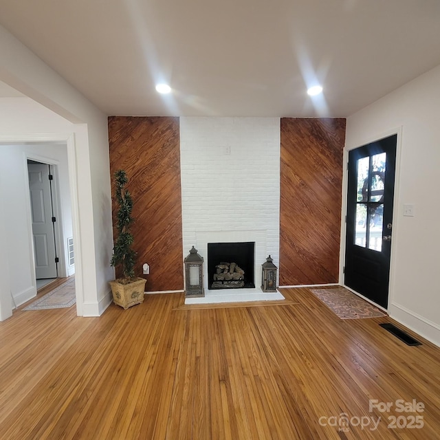 unfurnished living room featuring recessed lighting, visible vents, a large fireplace, wooden walls, and wood finished floors