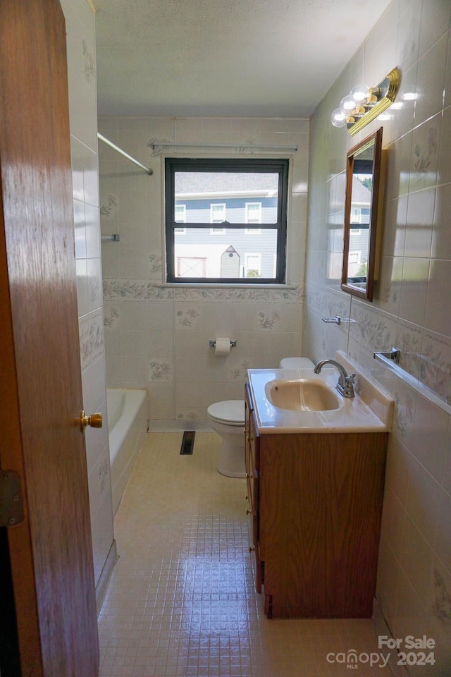 full bathroom with tile walls, tile patterned floors, vanity, tiled shower / bath, and toilet