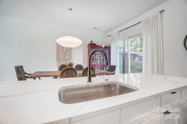 room details with pendant lighting, light stone countertops, white cabinets, and sink