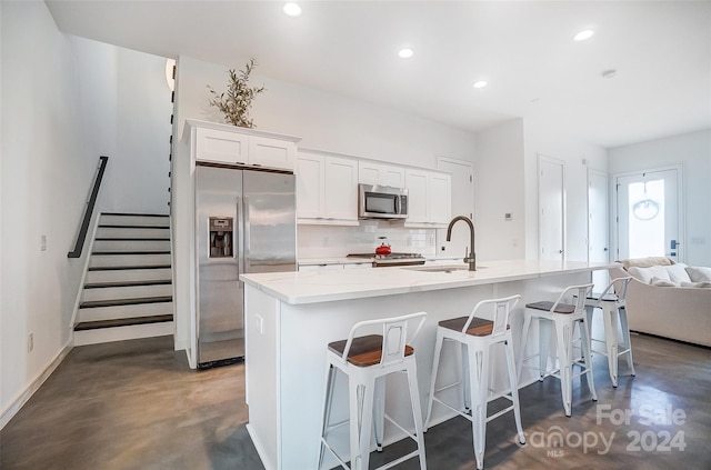 kitchen with a kitchen island with sink, appliances with stainless steel finishes, decorative backsplash, and white cabinetry