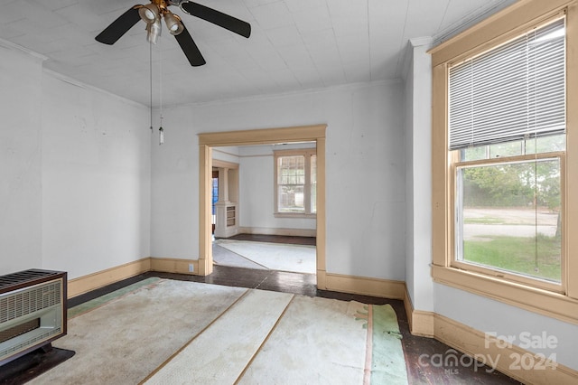 empty room with ornamental molding, heating unit, ceiling fan, and a healthy amount of sunlight