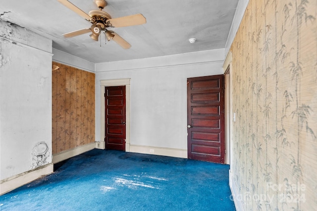 spare room featuring ceiling fan, wood walls, and dark colored carpet