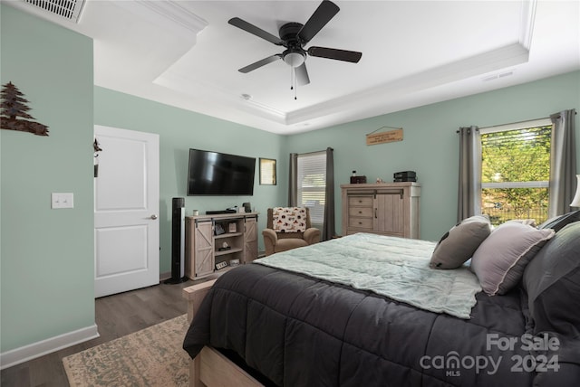 bedroom with ceiling fan, a tray ceiling, dark hardwood / wood-style floors, and multiple windows