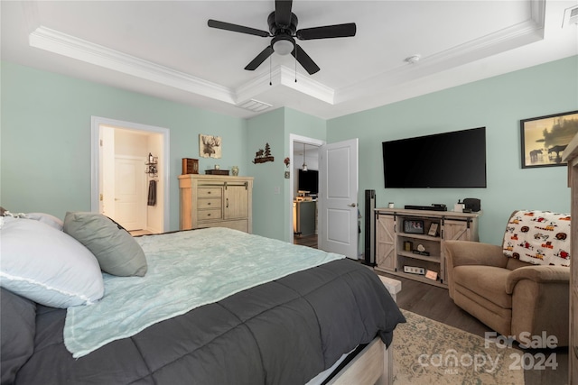 bedroom featuring ceiling fan, ensuite bath, a tray ceiling, and dark wood-type flooring