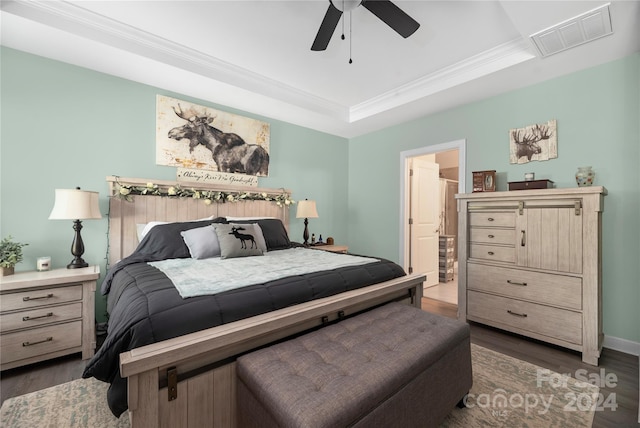 bedroom with ensuite bathroom, ceiling fan, a tray ceiling, dark hardwood / wood-style flooring, and ornamental molding