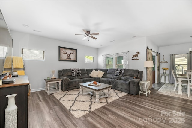 living room featuring a barn door, a ceiling fan, wood finished floors, baseboards, and visible vents