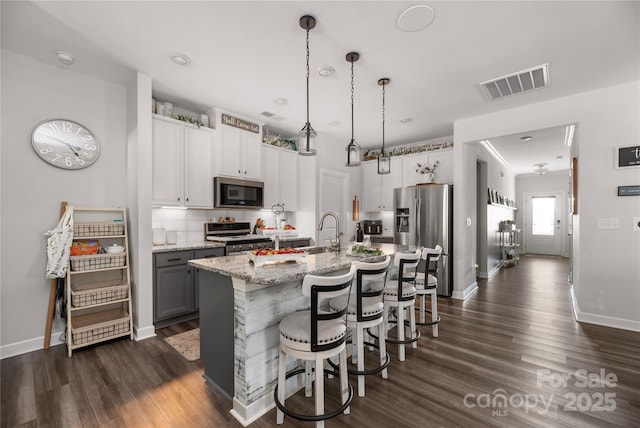 kitchen featuring dark wood-style flooring, appliances with stainless steel finishes, visible vents, and a breakfast bar area
