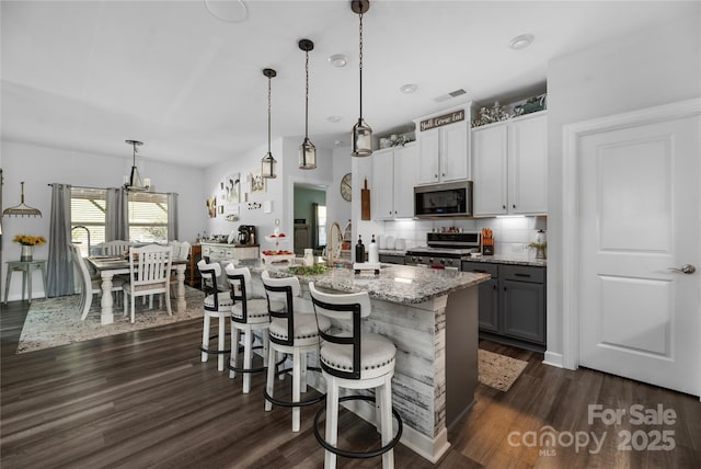 kitchen with stainless steel appliances, visible vents, light stone counters, and dark wood finished floors