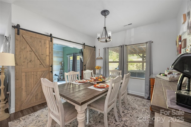 dining space with a barn door, wood finished floors, visible vents, and a notable chandelier