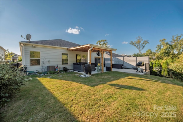 back of house featuring a lawn, a patio area, a fenced backyard, and a hot tub
