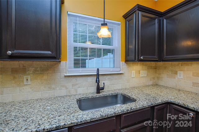 kitchen featuring dark brown cabinets, decorative light fixtures, sink, light stone countertops, and backsplash