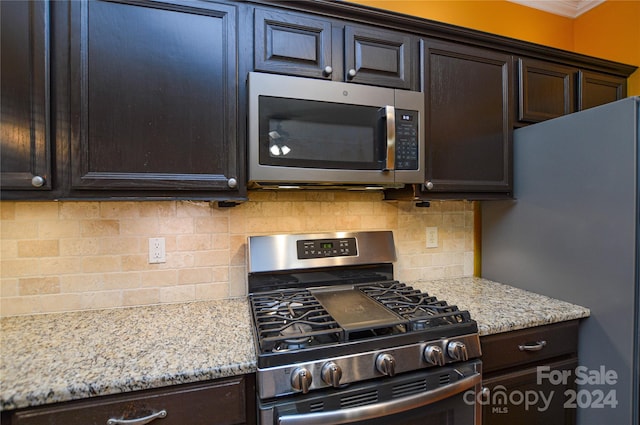 kitchen with light stone counters, appliances with stainless steel finishes, backsplash, and dark brown cabinetry