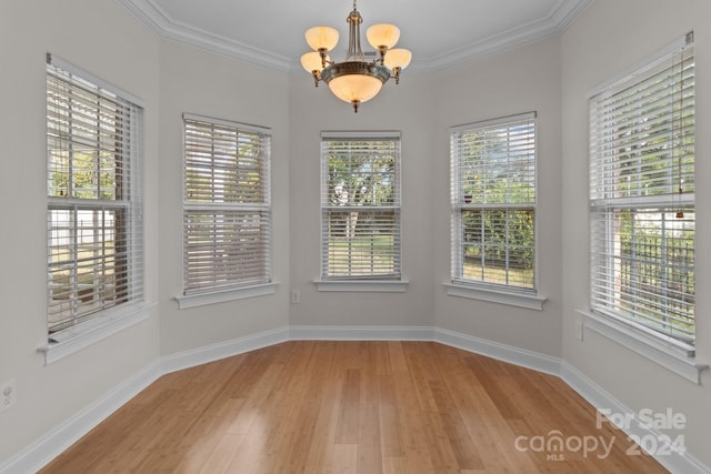 unfurnished dining area featuring wood-type flooring, an inviting chandelier, crown molding, and a healthy amount of sunlight