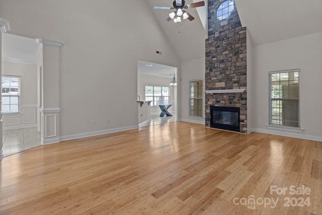 unfurnished living room with visible vents, a high ceiling, a stone fireplace, ceiling fan, and wood finished floors