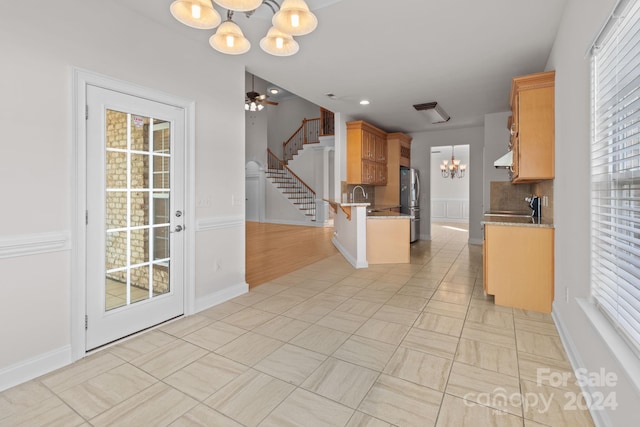 kitchen with sink, ceiling fan with notable chandelier, stainless steel refrigerator, decorative backsplash, and decorative light fixtures