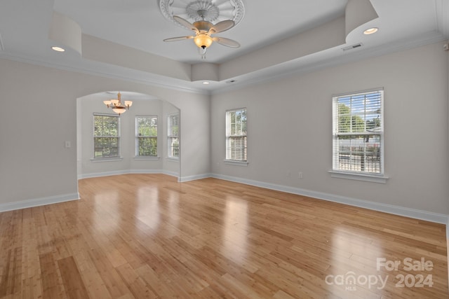spare room featuring arched walkways, a healthy amount of sunlight, a raised ceiling, light wood finished floors, and baseboards